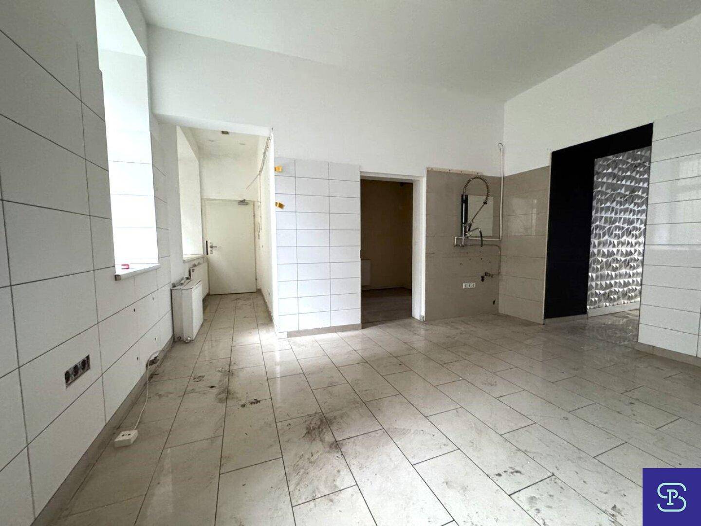 Helle, geflieste Küche mit Fenstern und Heizkörper, bereit für die Installation von Geräten.