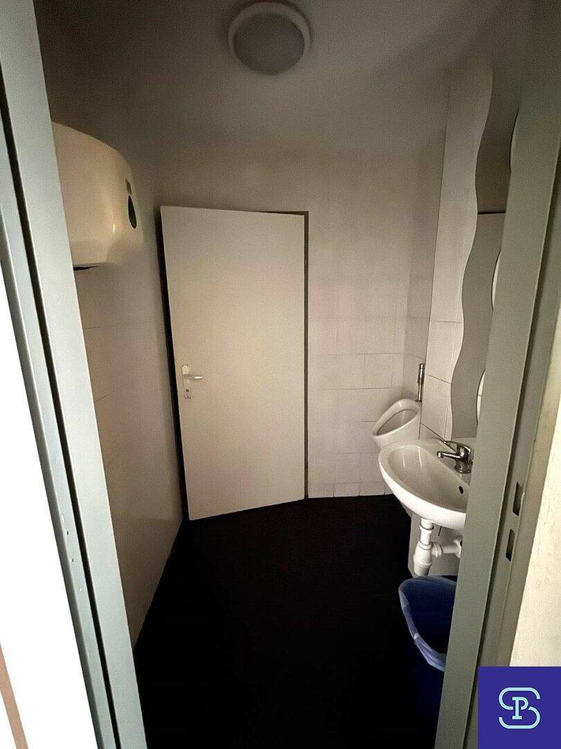 Toilettenraum mit Urinal, Waschbecken und weiß gefliesten Wänden.