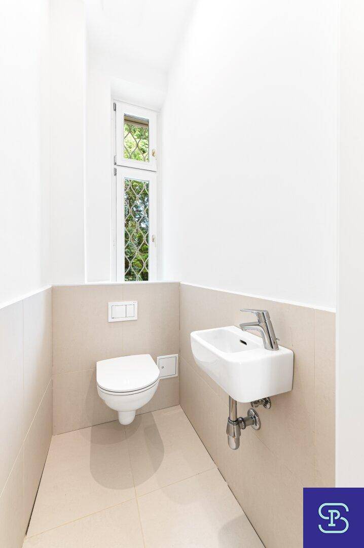 Modernes Gäste-WC mit wandhängendem WC und kleinem Waschbecken, hell gefliest.