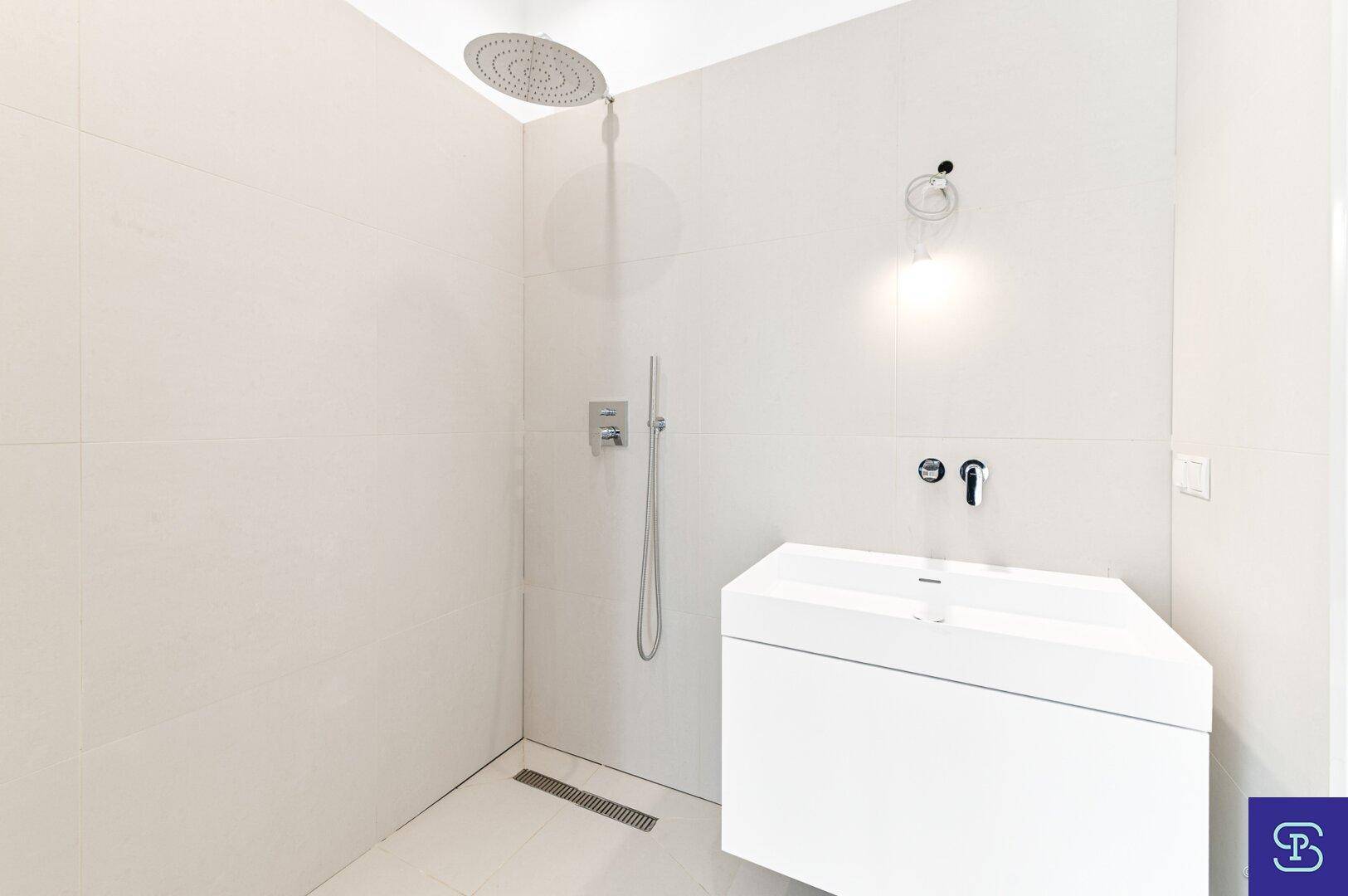 Modernes Badezimmer mit ebenerdiger Dusche und weißem Waschtisch, minimalistisch gestaltet.