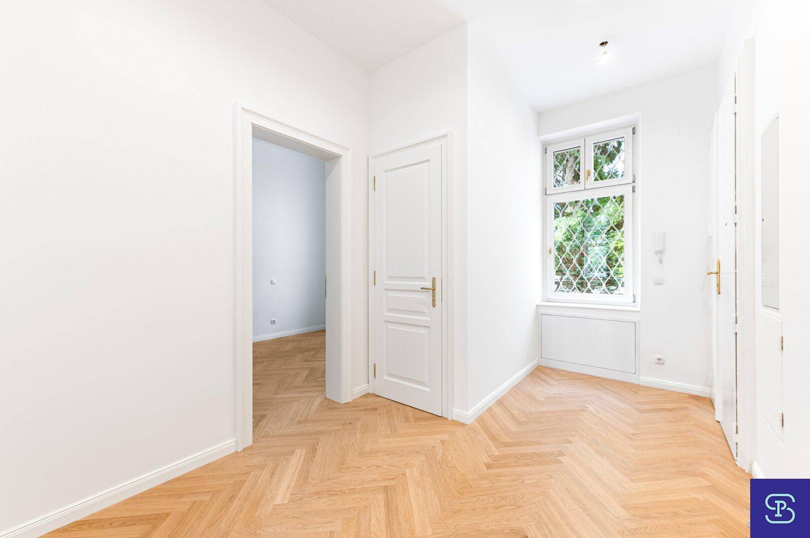 Heller Flur mit Fischgrätparkett und Fenster, verbindet die verschiedenen Räume der Wohnung.