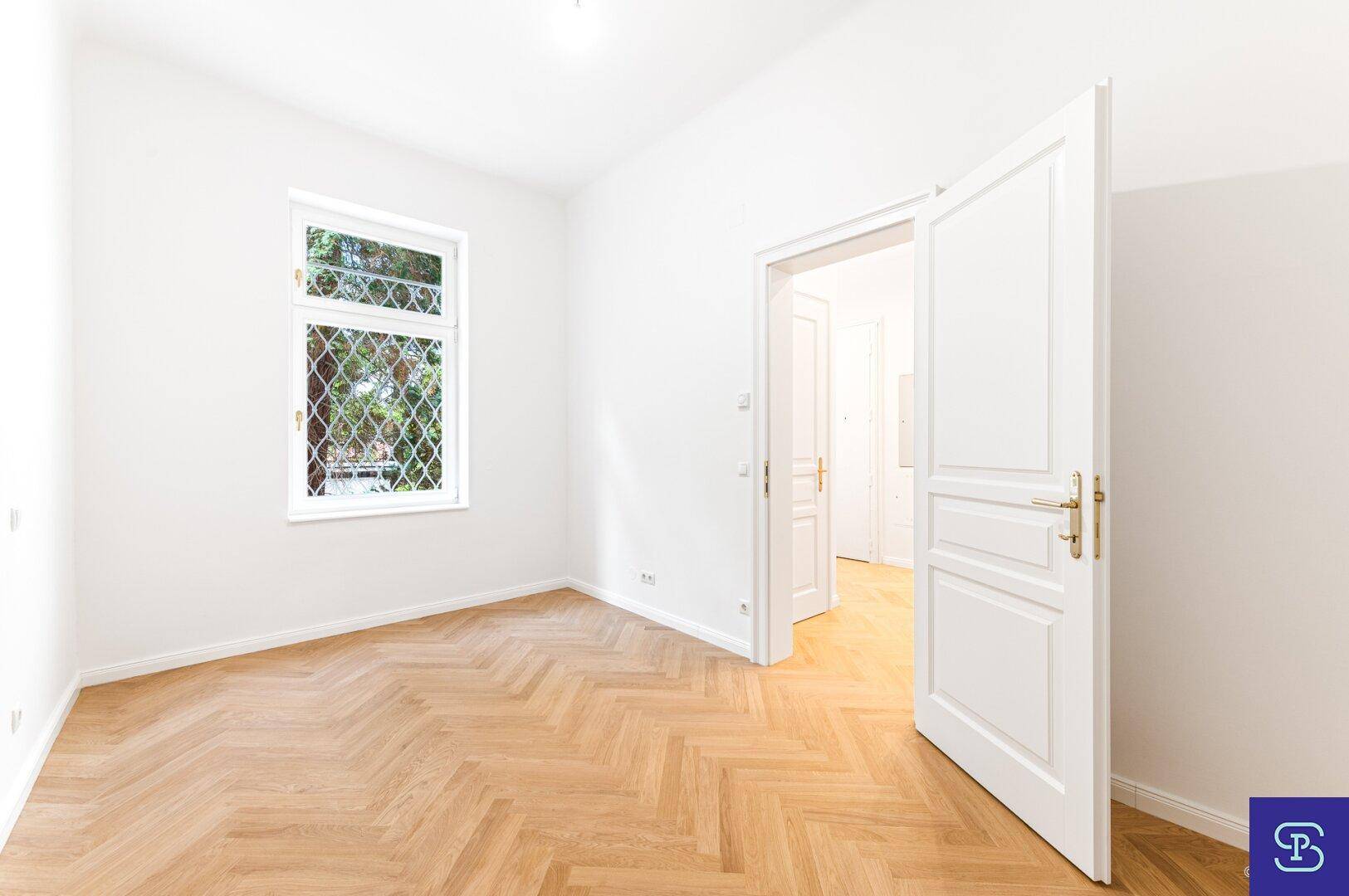Helles Zimmer mit Fischgrätparkett und weißer Tür, bietet eine ruhige Atmosphäre.