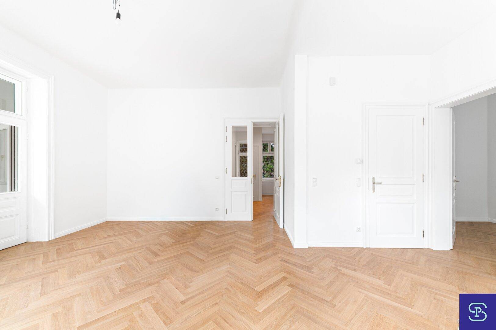 Großes, helles Zimmer mit Fischgrätparkett und mehreren Türen, bietet flexible Raumgestaltung.