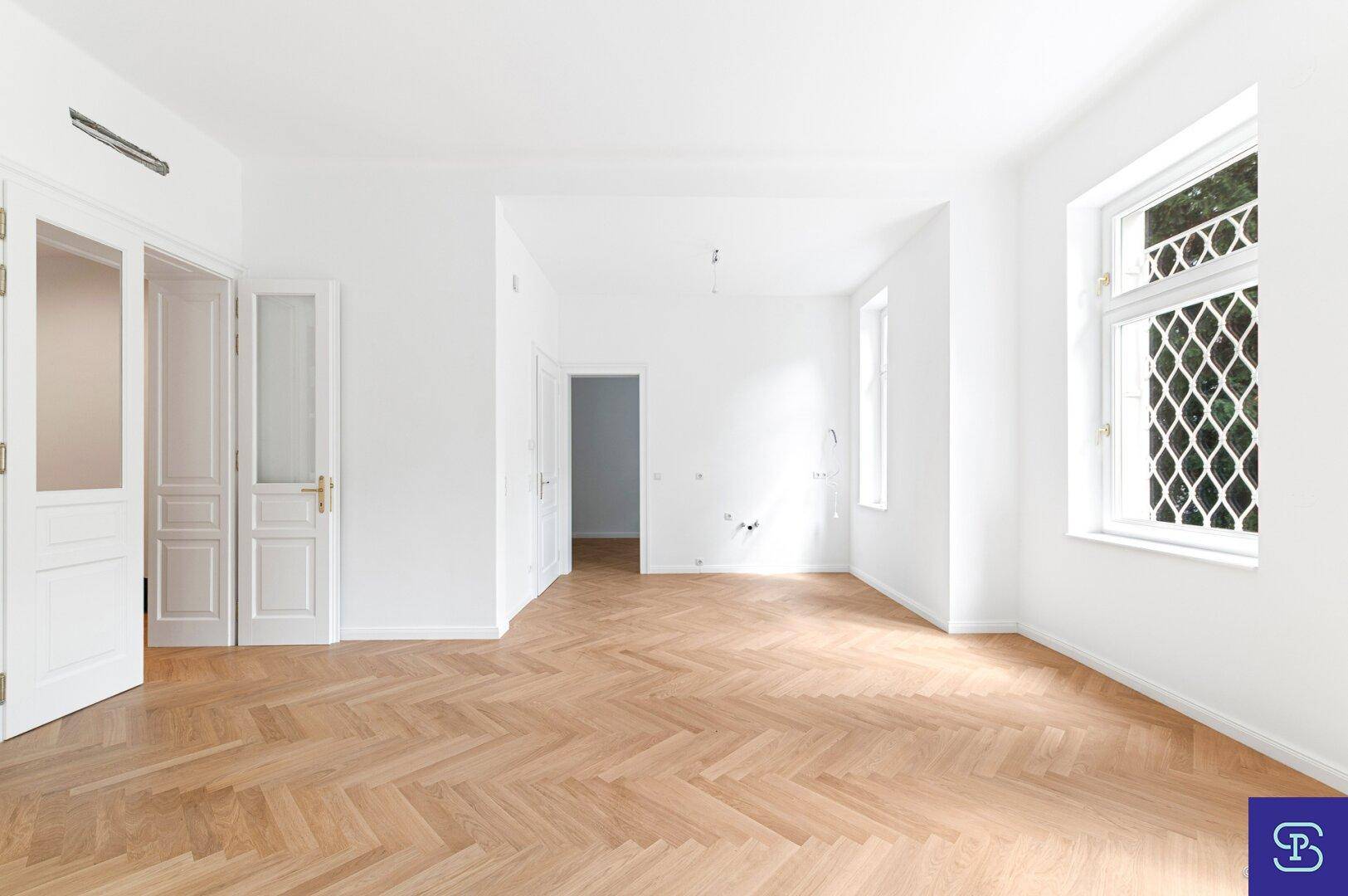 Geräumiges, helles Zimmer mit Fischgrätparkett und weißen Türen, ideal für Wohn- oder Essbereich.