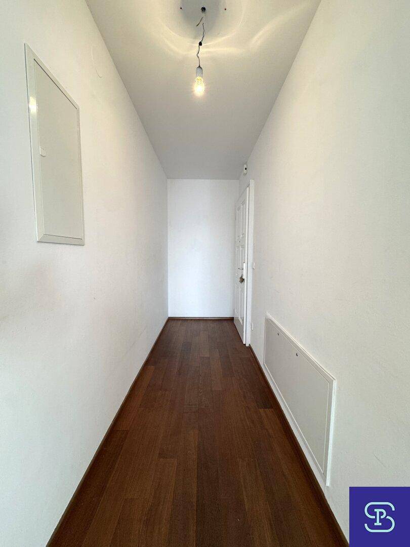 Eingangsbereich mit Holzboden und weiß gestrichenen Wänden, führt zur Wohnungstür.