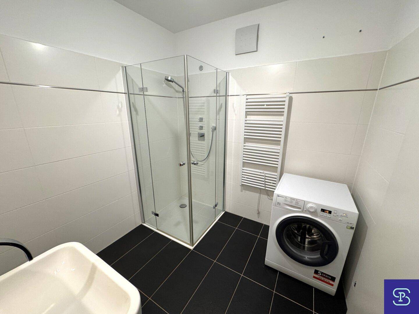 Praktisches Badezimmer mit Dusche, Waschmaschine und beheiztem Handtuchhalter.