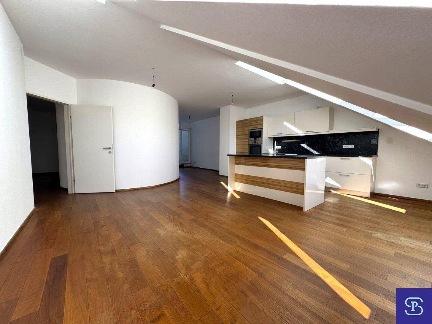 Geräumiger offener Wohnbereich mit Holzboden und moderner Küche im Hintergrund.