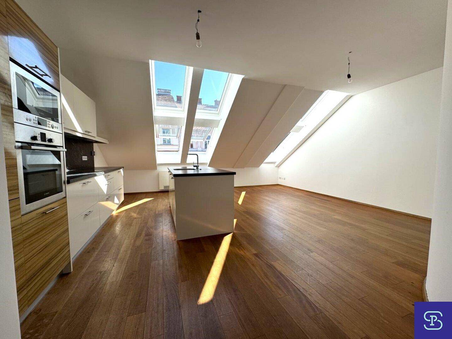 Offener Küchenbereich mit Holzboden und viel Tageslicht durch die schrägen Dachfenster.