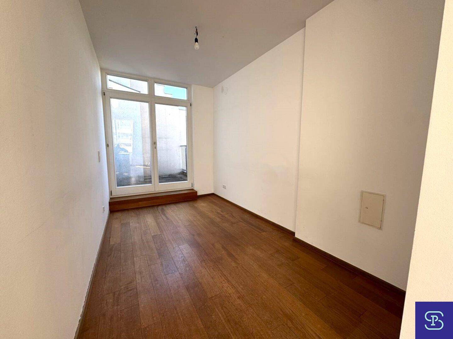 Kleiner Raum mit Holzboden und Zugang zu einem Außenbereich durch eine Glastür.