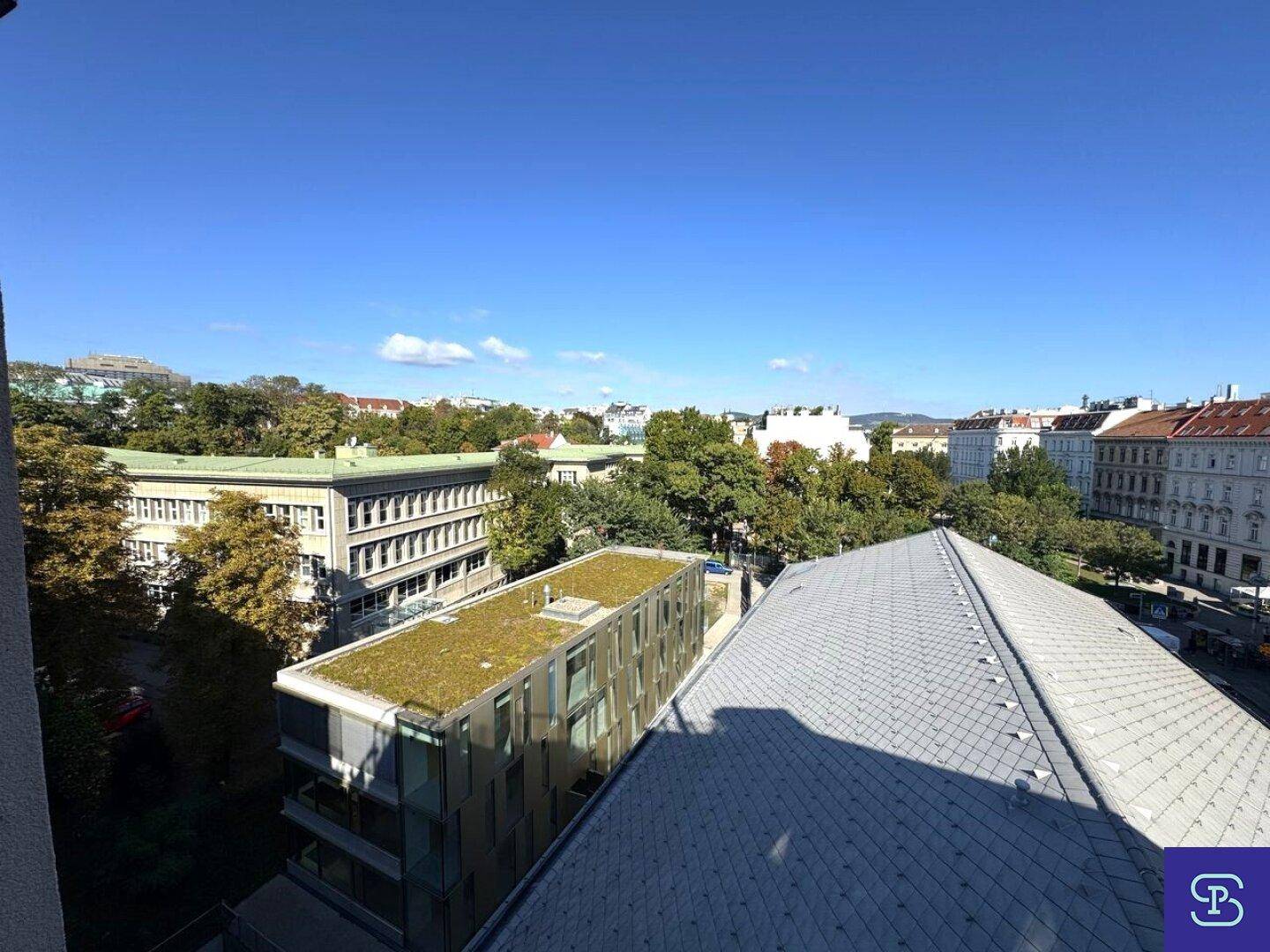 Weitblick über die Stadt mit grünen Dächern und umliegenden Gebäuden an einem sonnigen Tag.