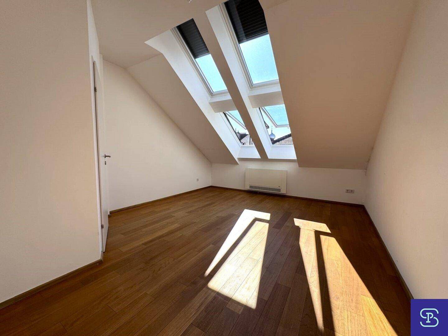 Helles Zimmer mit Holzboden und schrägen Dachfenstern, ideal als Schlaf- oder Arbeitszimmer.