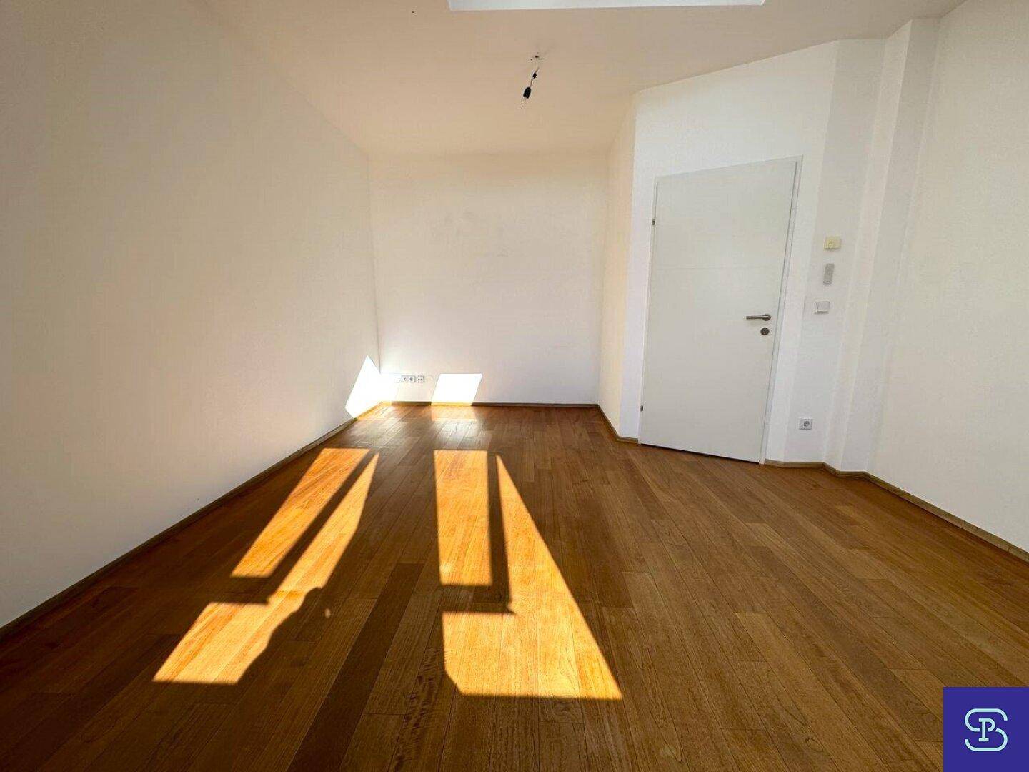 Leerer Raum mit Holzboden und viel Sonnenlicht, geeignet für verschiedene Nutzungen.