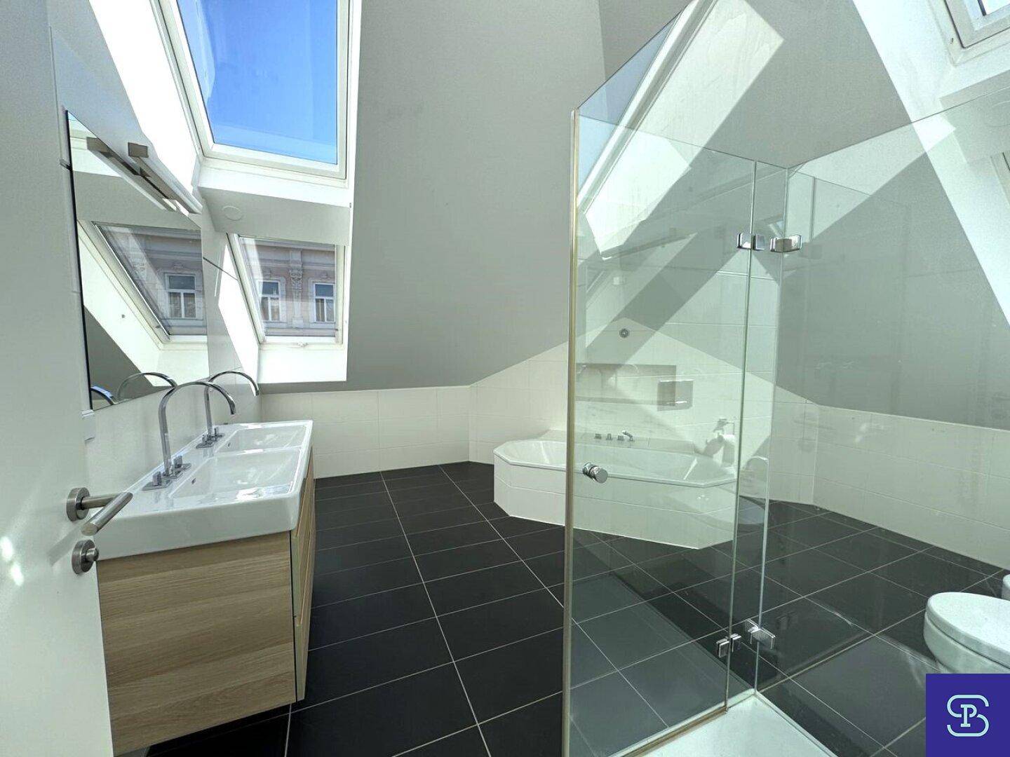Modernes Badezimmer mit dunklen Fliesen, Doppelwaschbecken und großer Glasdusche unter Dachfenstern.