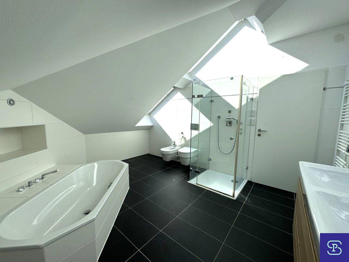 Geräumiges Badezimmer mit Badewanne, Glasdusche, Bidet und viel Tageslicht durch Dachfenster.