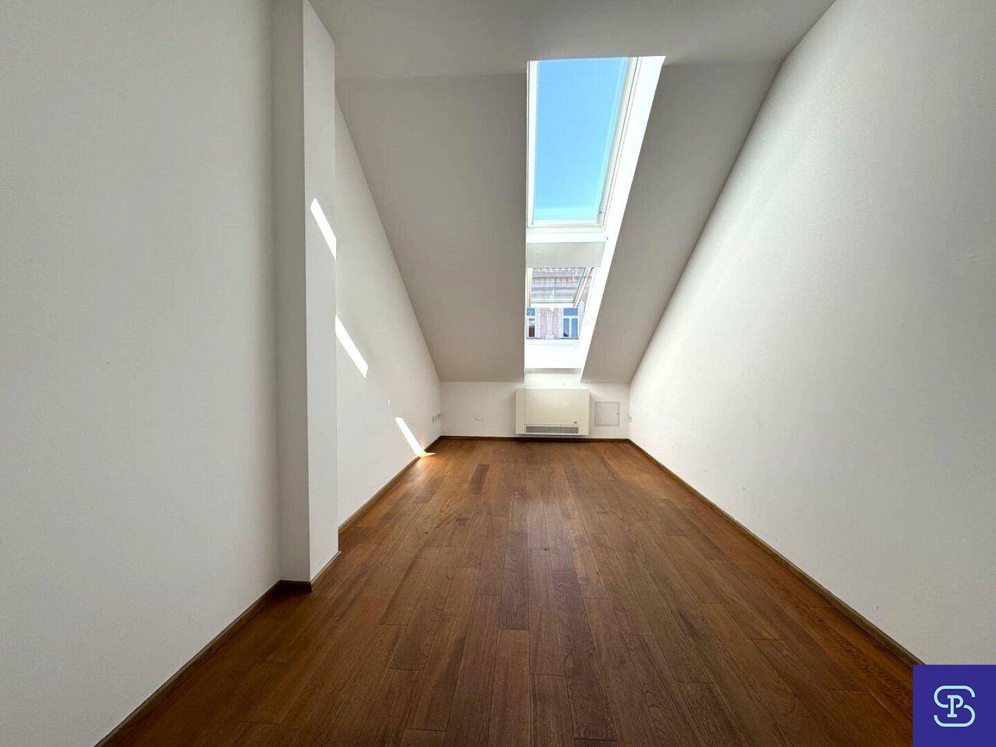 Ruhiges Zimmer mit Holzboden und einem einzelnen Dachfenster, ideal als Schlafzimmer.
