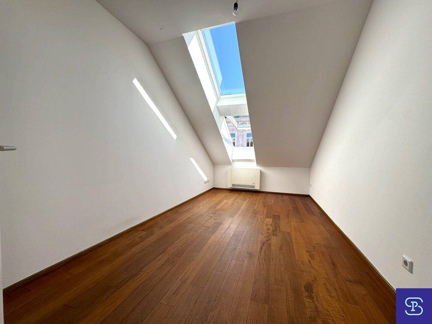 Helles Zimmer mit Holzboden und schrägem Dachfenster, bietet viel Tageslicht.