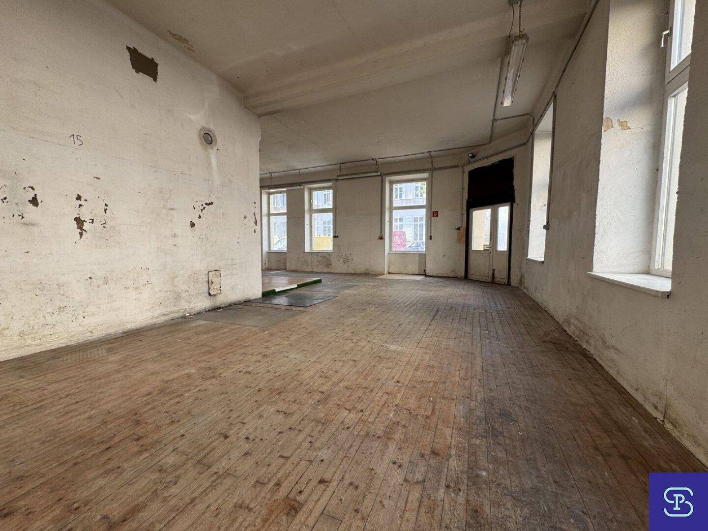 Weiterer Blick in den großen Gewerberaum mit abblätternder Farbe an den Wänden und Holzdielenboden.