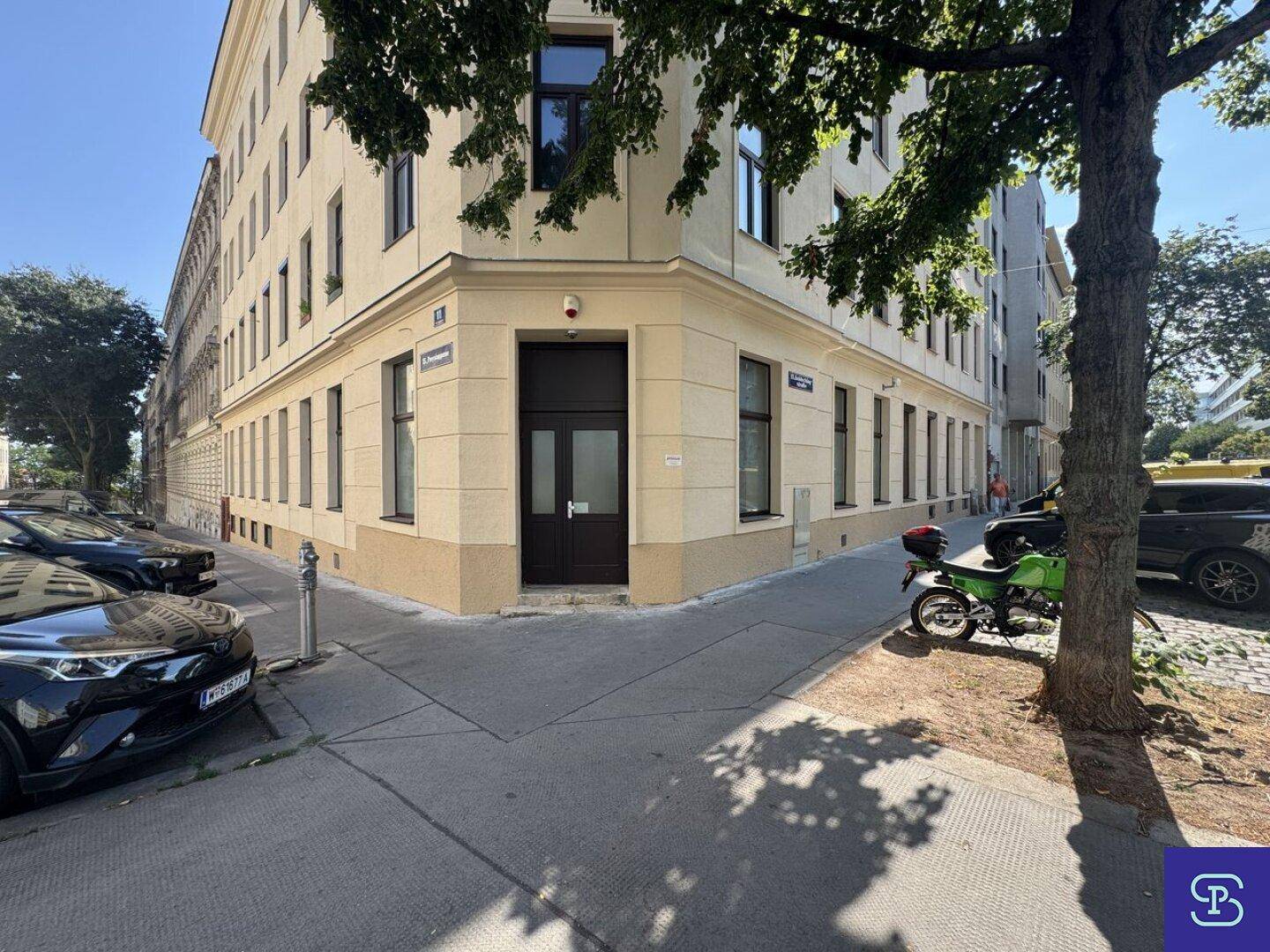 Eckgebäude mit beiger Fassade, vielen Fenstern und einer Eingangstür an der Straßenecke.