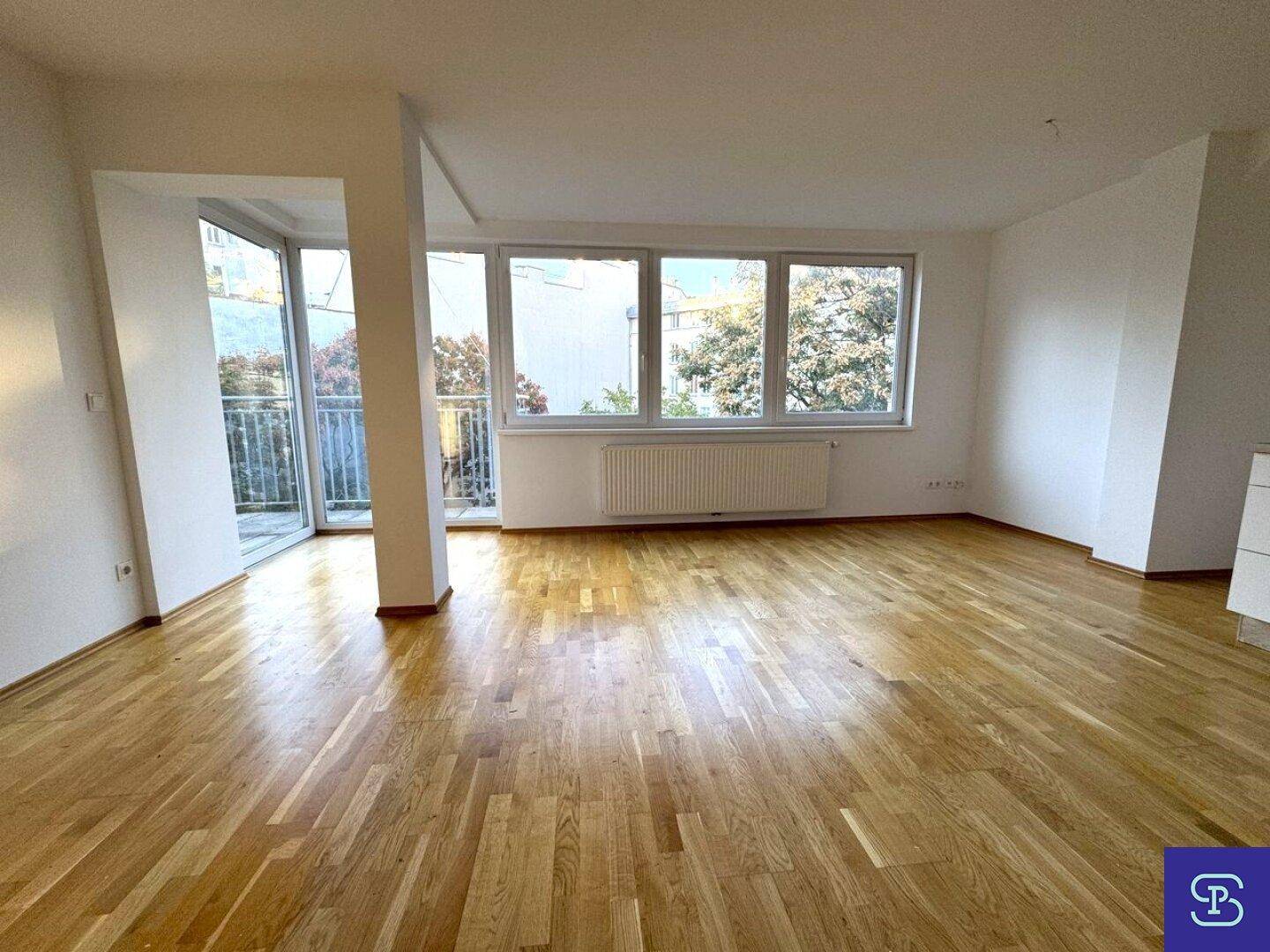 Geräumiges Wohnzimmer mit hellem Holzboden, großen Fenstern und direktem Zugang zum Außenbereich.