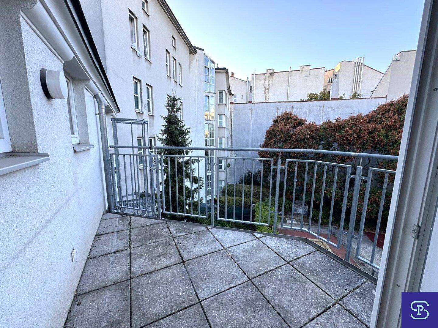 Kleiner Balkon mit Fliesenboden und Metallgeländer, bietet Blick auf den begrünten Innenhof.
