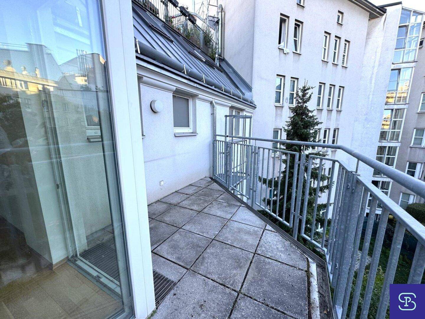 Blick vom Balkon auf die Gebäudefassade und angrenzende Außenbereiche mit Metallgeländer.