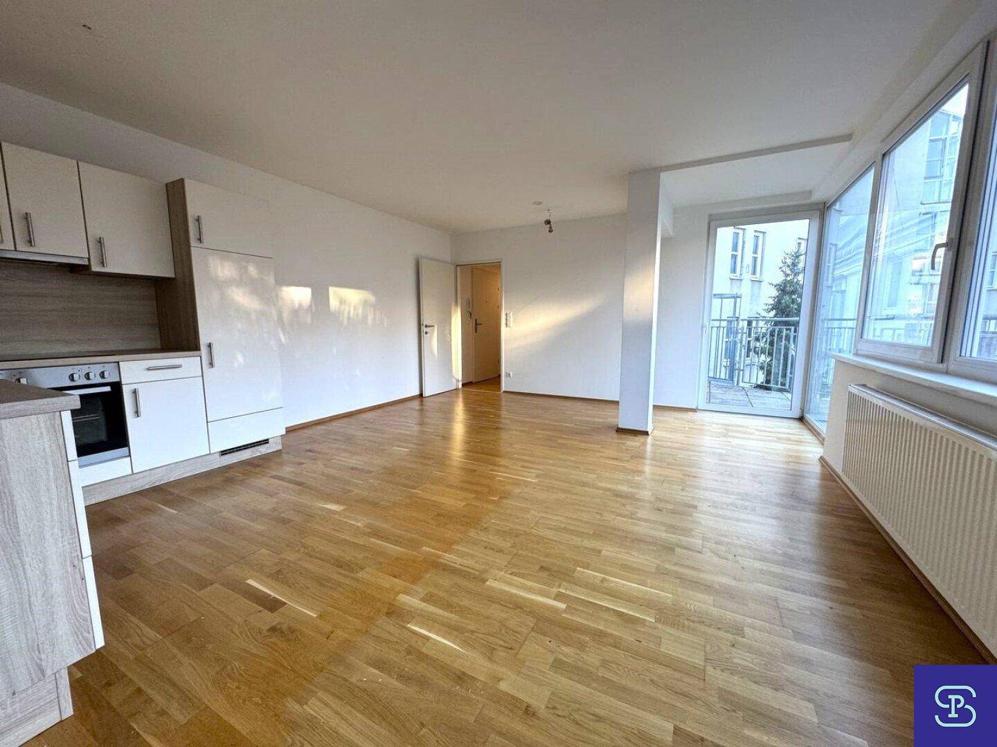 Heller Wohnbereich mit integrierter Küchenzeile, Holzboden und Zugang zum Balkon.