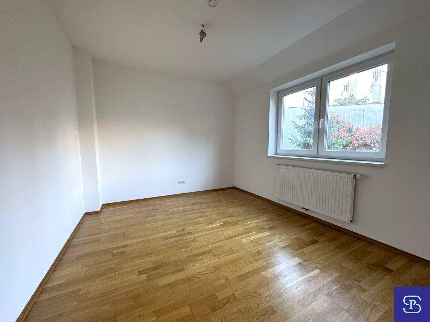 Helles Schlafzimmer mit Holzboden und einem Fenster, das Tageslicht hereinlässt.