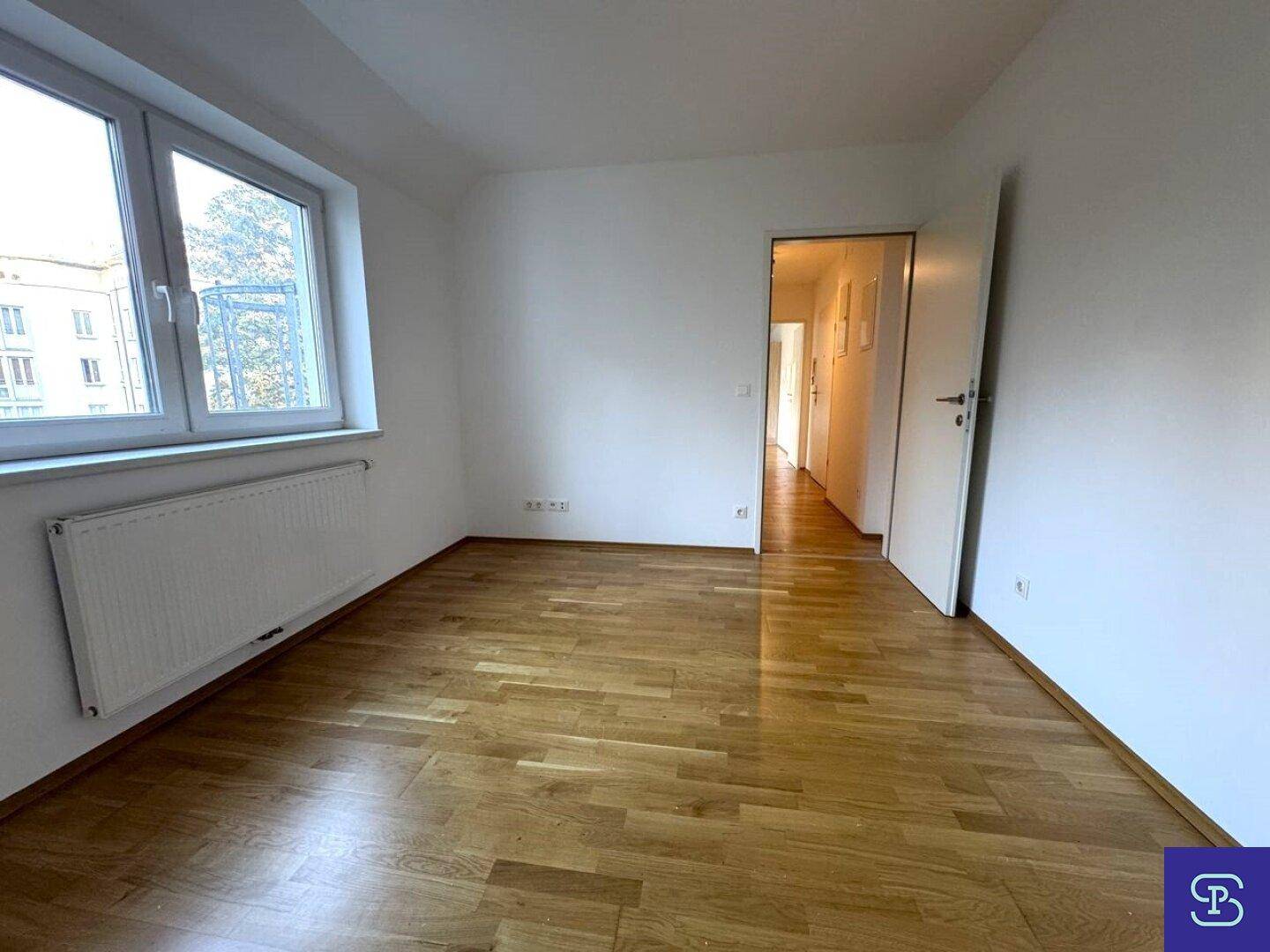 Geräumiges Schlafzimmer mit Holzboden, Fenster und Zugang zum Flur der Wohnung.