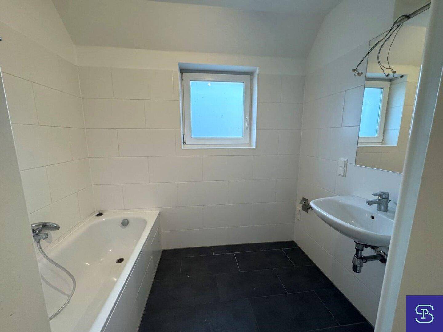 Modernes Badezimmer mit weißen Wandfliesen, dunklem Boden und Badewanne sowie Waschbecken.