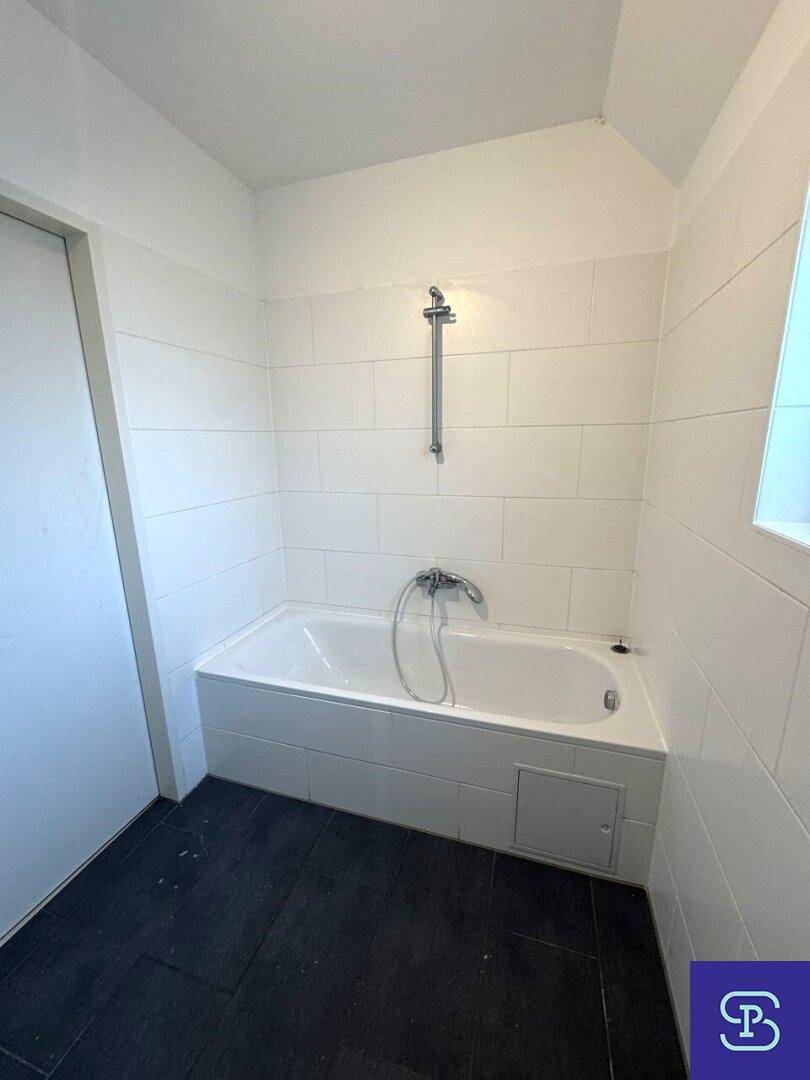 Badezimmer mit eingebauter Badewanne und Duschvorrichtung, umgeben von weißen Fliesen.
