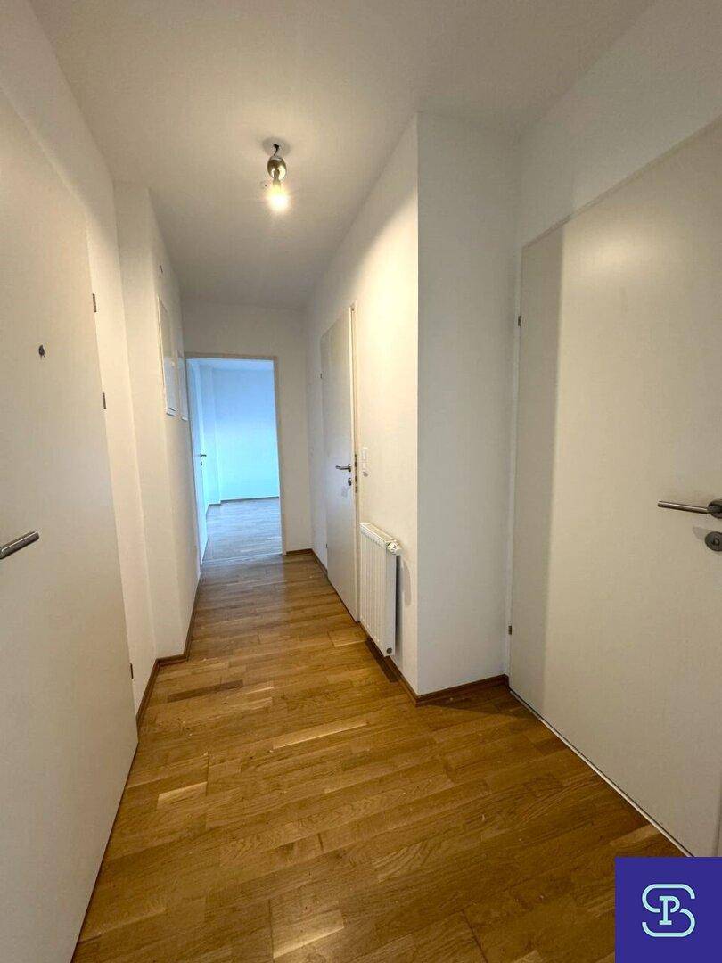 Langer Flur mit Holzboden und weißen Wänden, der die verschiedenen Räume verbindet.