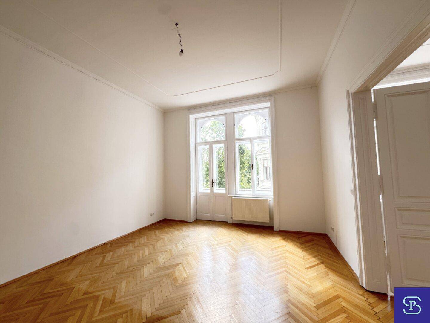 Geräumiges Zimmer mit klassischem Fischgrätparkett und großen Fenstern, die den Raum erhellen.