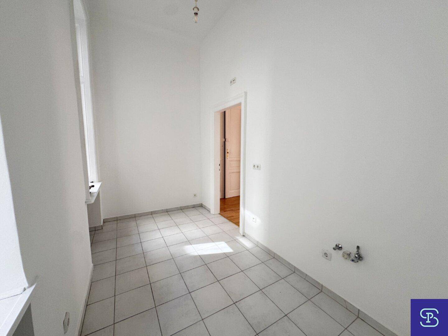 Leerer Raum mit Fliesenboden und Fenster, vorbereitet für die Installation einer Küche.