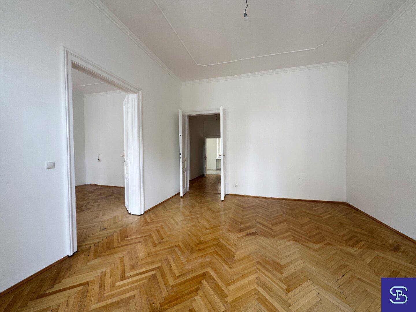 Geräumiges Zimmer mit Fischgrätparkett und offenen Türen zu angrenzenden Bereichen.