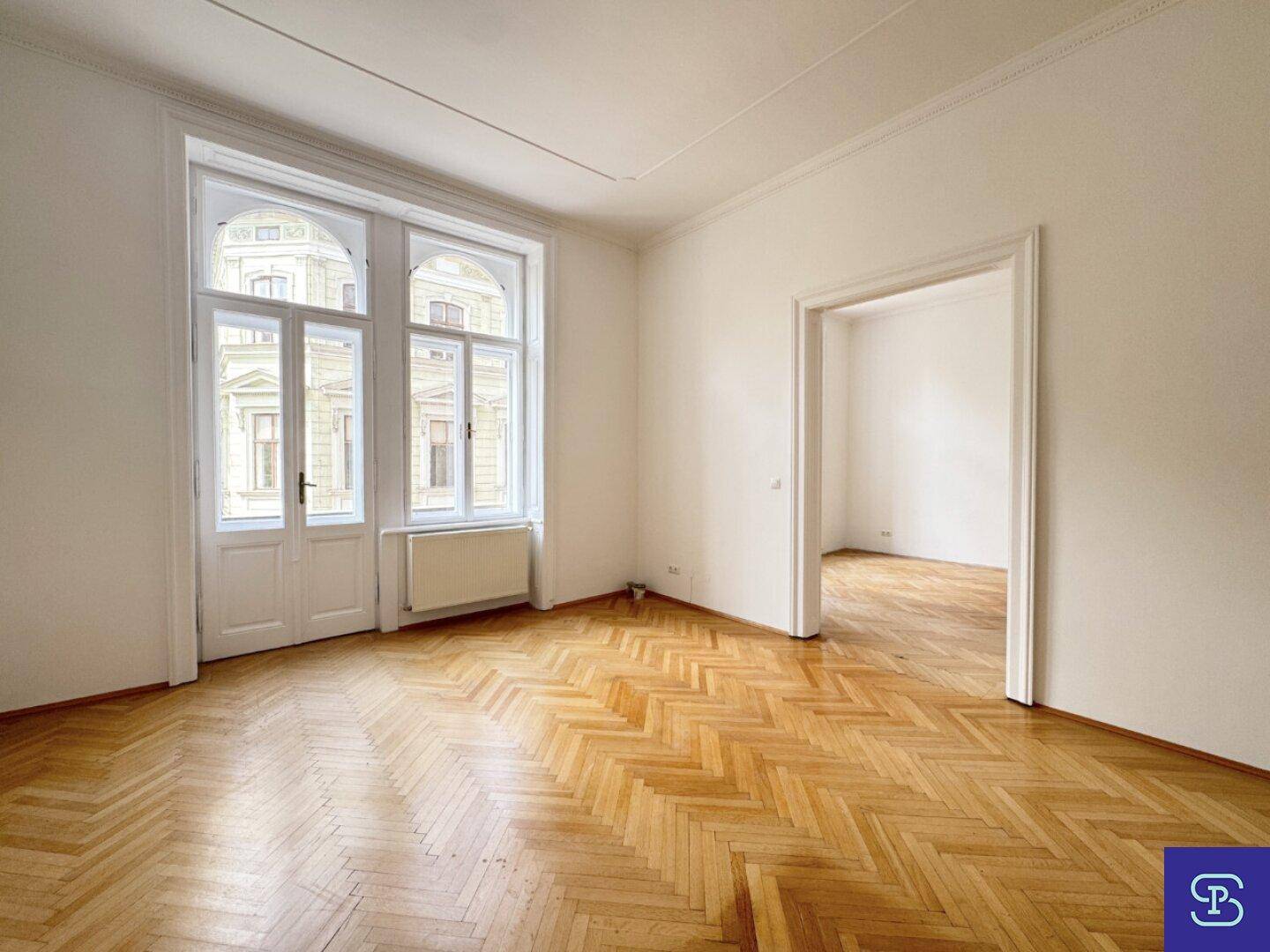 Lichtdurchflutetes Zimmer mit elegantem Fischgrätparkett und hohen Fenstern, die eine angenehme Atmosphäre schaffen.