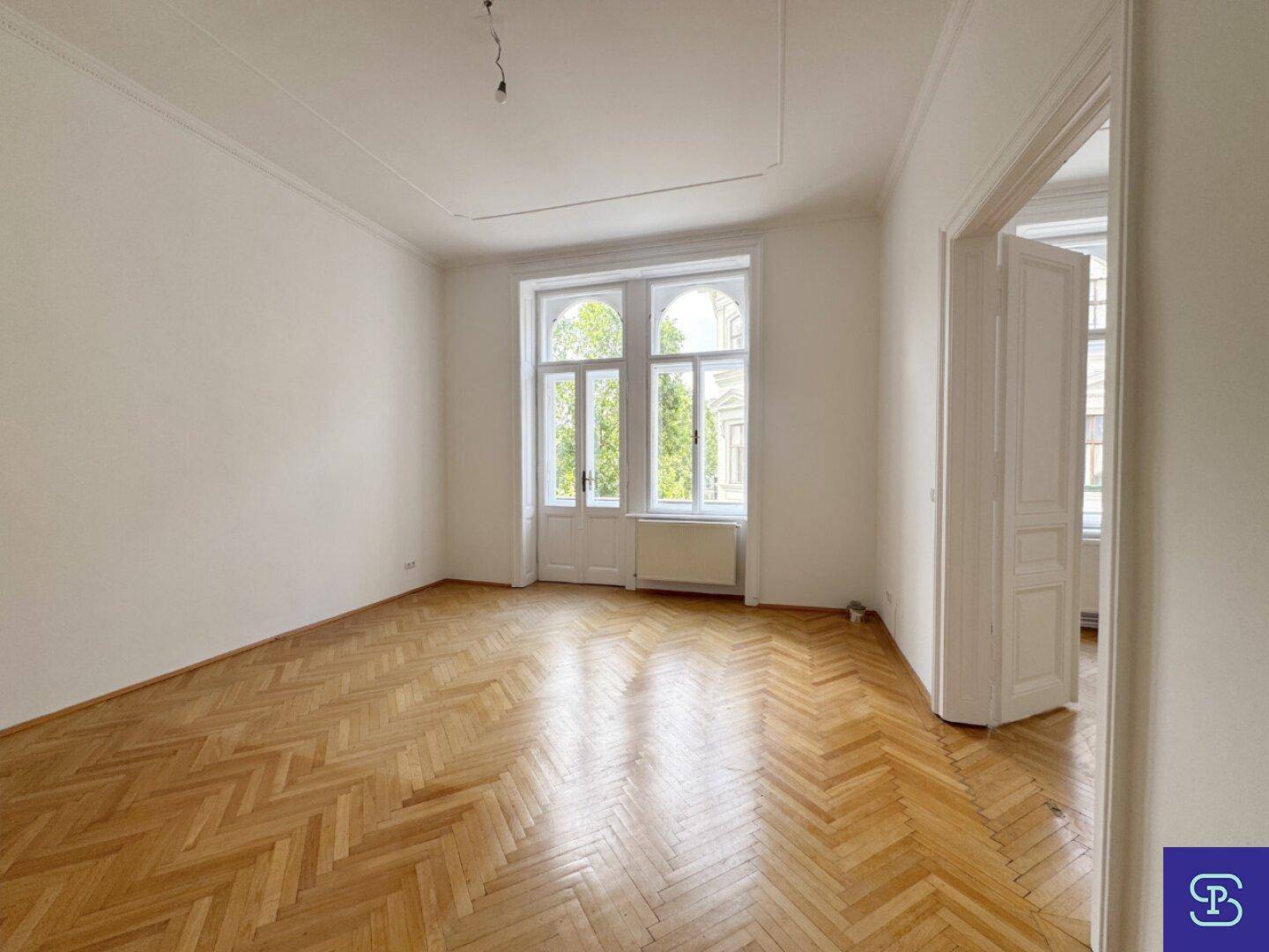 Großzügiges Zimmer mit klassischem Fischgrätparkett und hohen Fenstern, die viel Licht spenden.