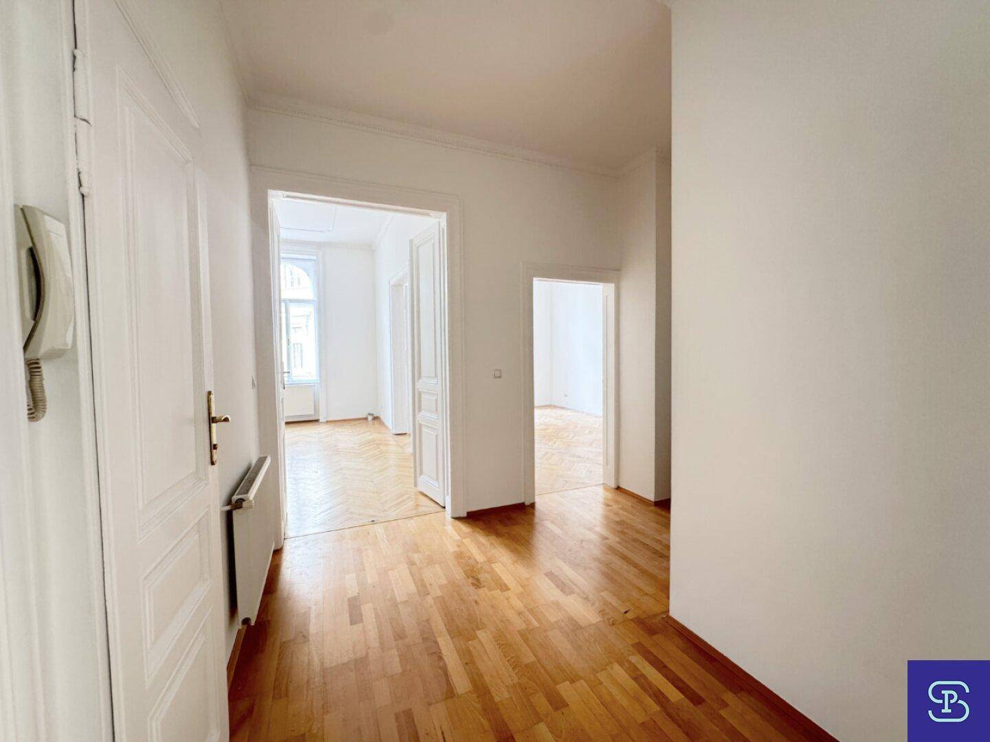 Geräumiger Flur mit Holzboden und weißen Wänden, der Zugang zu verschiedenen Zimmern bietet.