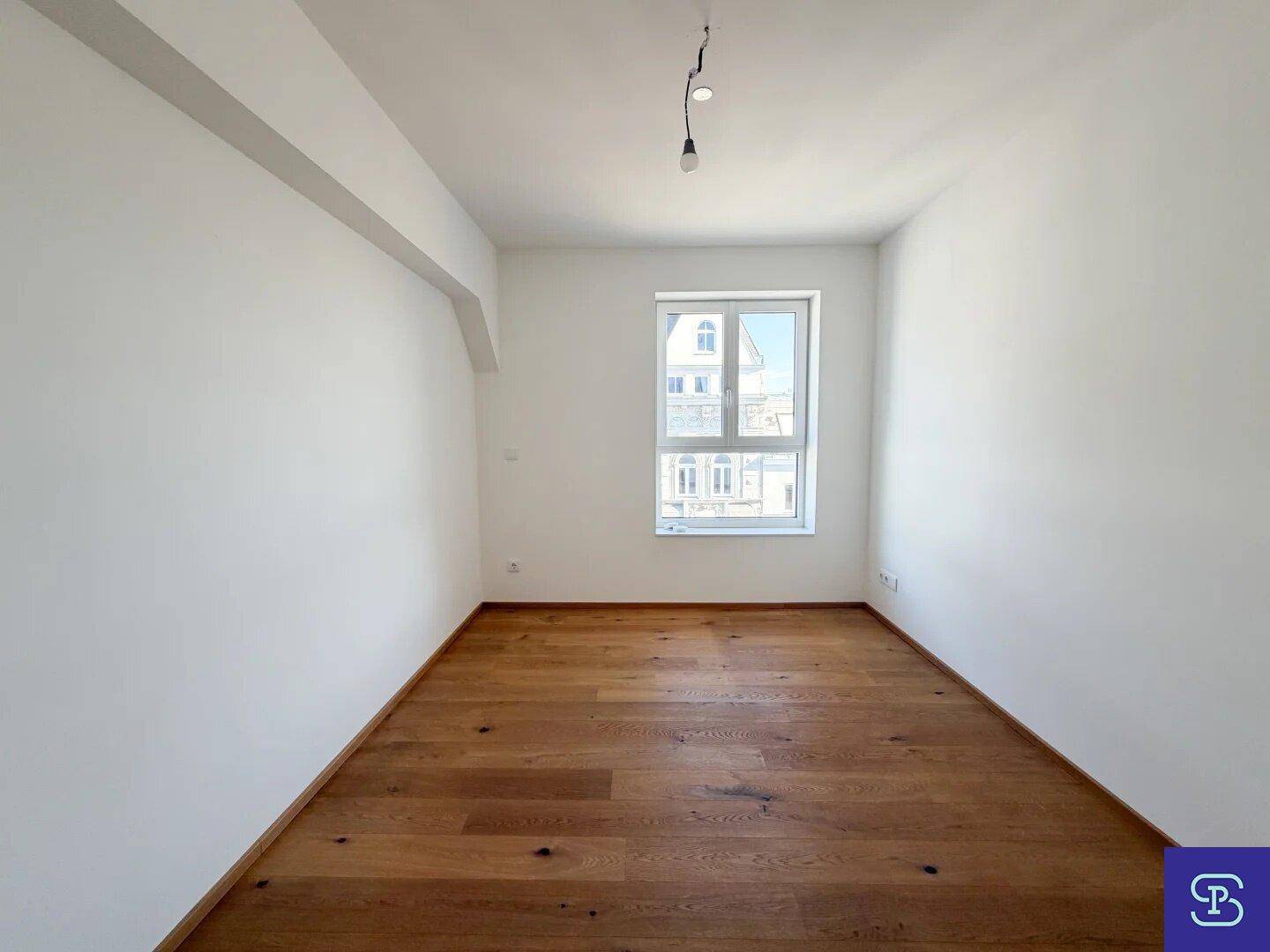 Helles Zimmer mit Holzboden und einem Fenster, bereit zur individuellen Gestaltung.