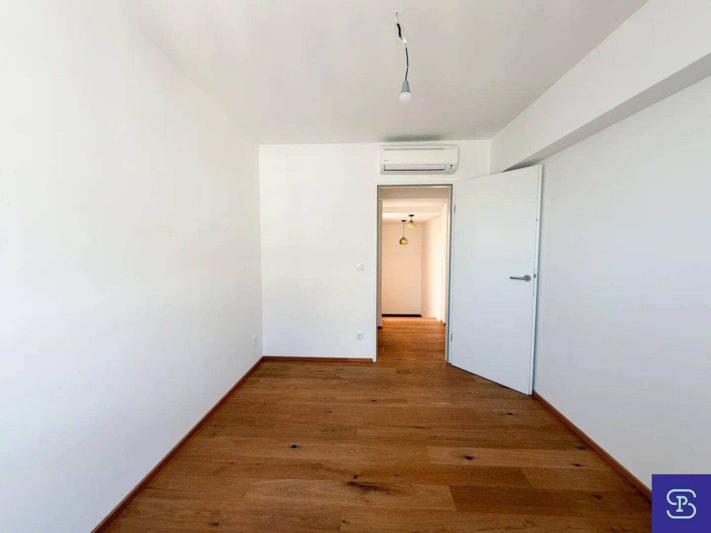 Leeres Zimmer mit Holzboden und Klimaanlage, ideal als Schlaf- oder Arbeitszimmer.