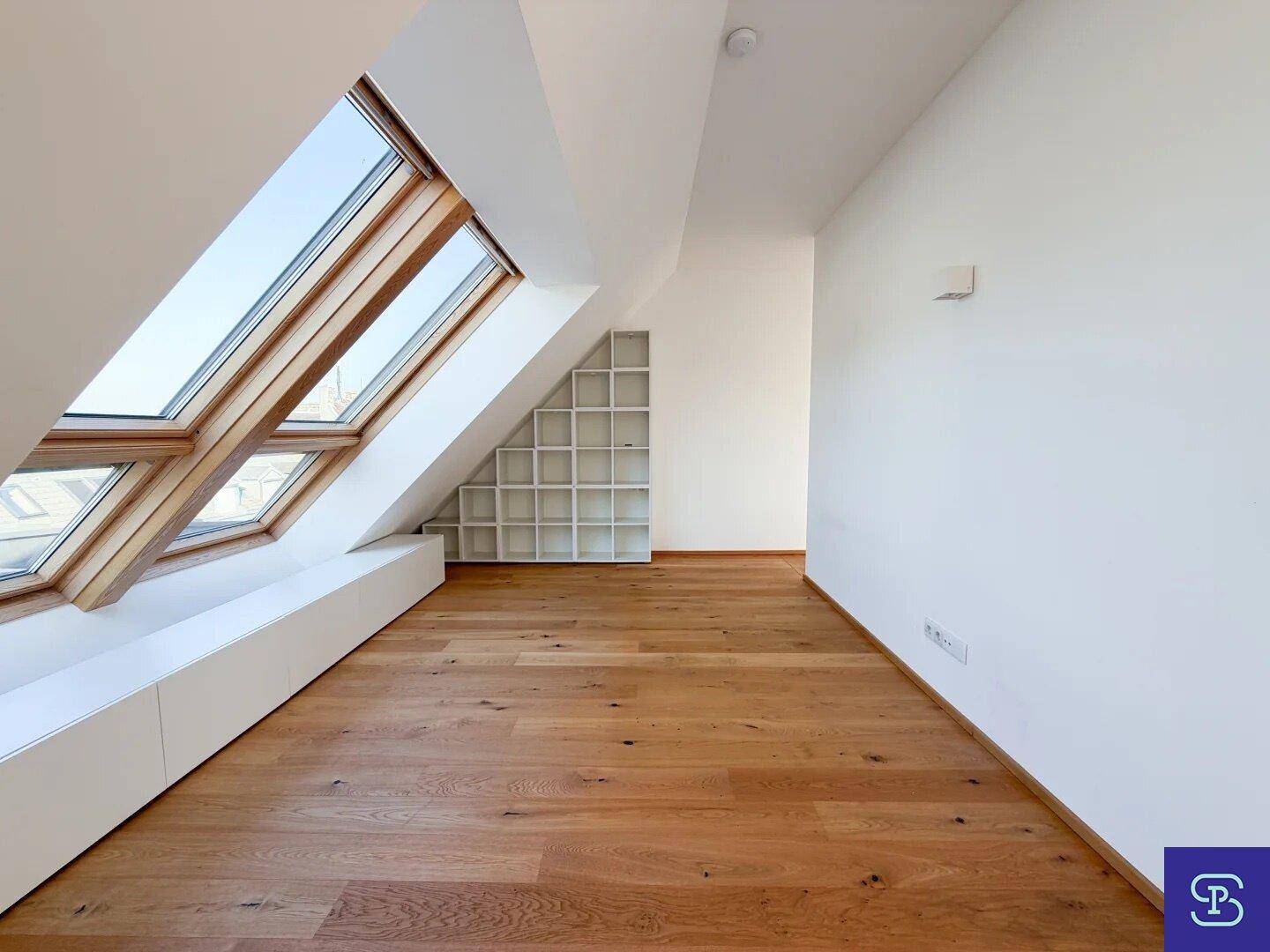 Helles Dachzimmer mit Holzboden, großen Dachfenstern und integriertem Regal.