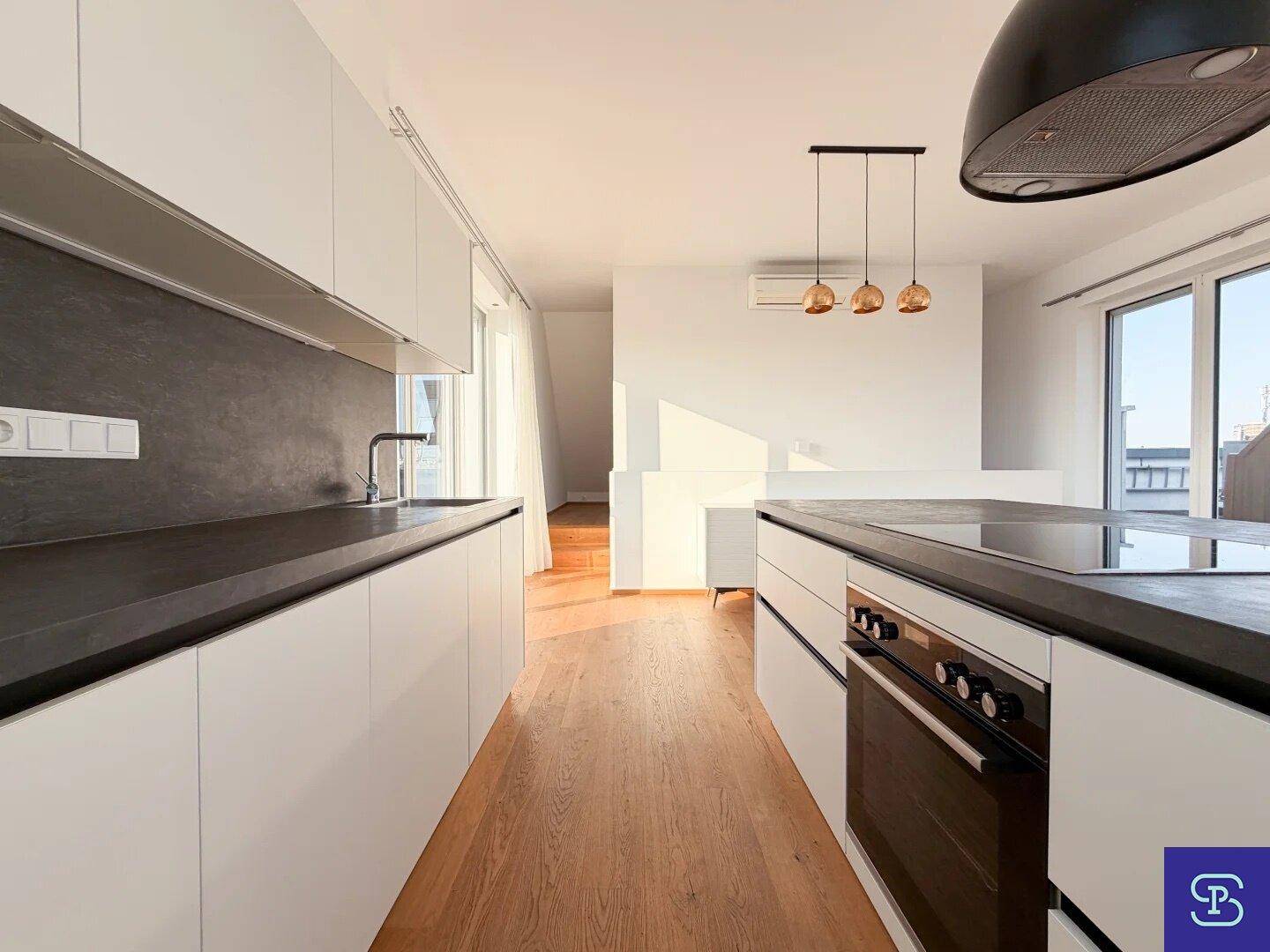 Moderne Einbauküche mit weißen Schränken, dunkler Arbeitsplatte und integriertem Backofen.