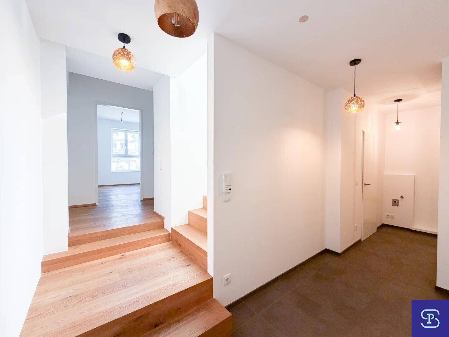 Heller Flur mit Holztreppe, kombiniertem Fliesen- und Holzboden und modernen Leuchten.