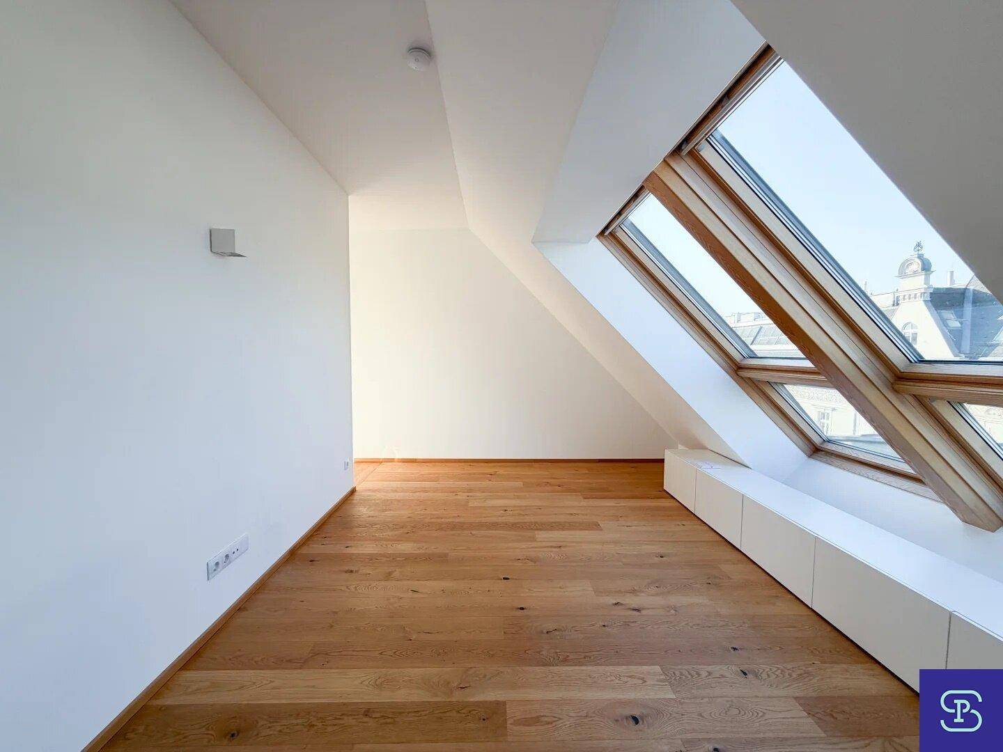 Helles Dachzimmer mit Holzboden, großen Dachfenstern und viel natürlichem Licht.