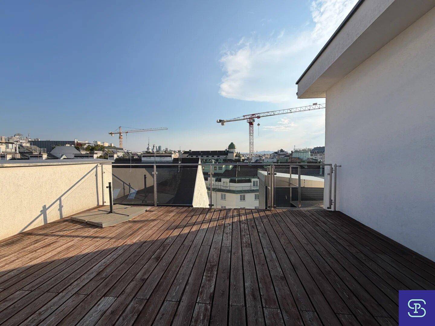 Weitläufige Dachterrasse mit Holzbelag und Glasgeländer, bietet einen Panoramablick über die Stadt.