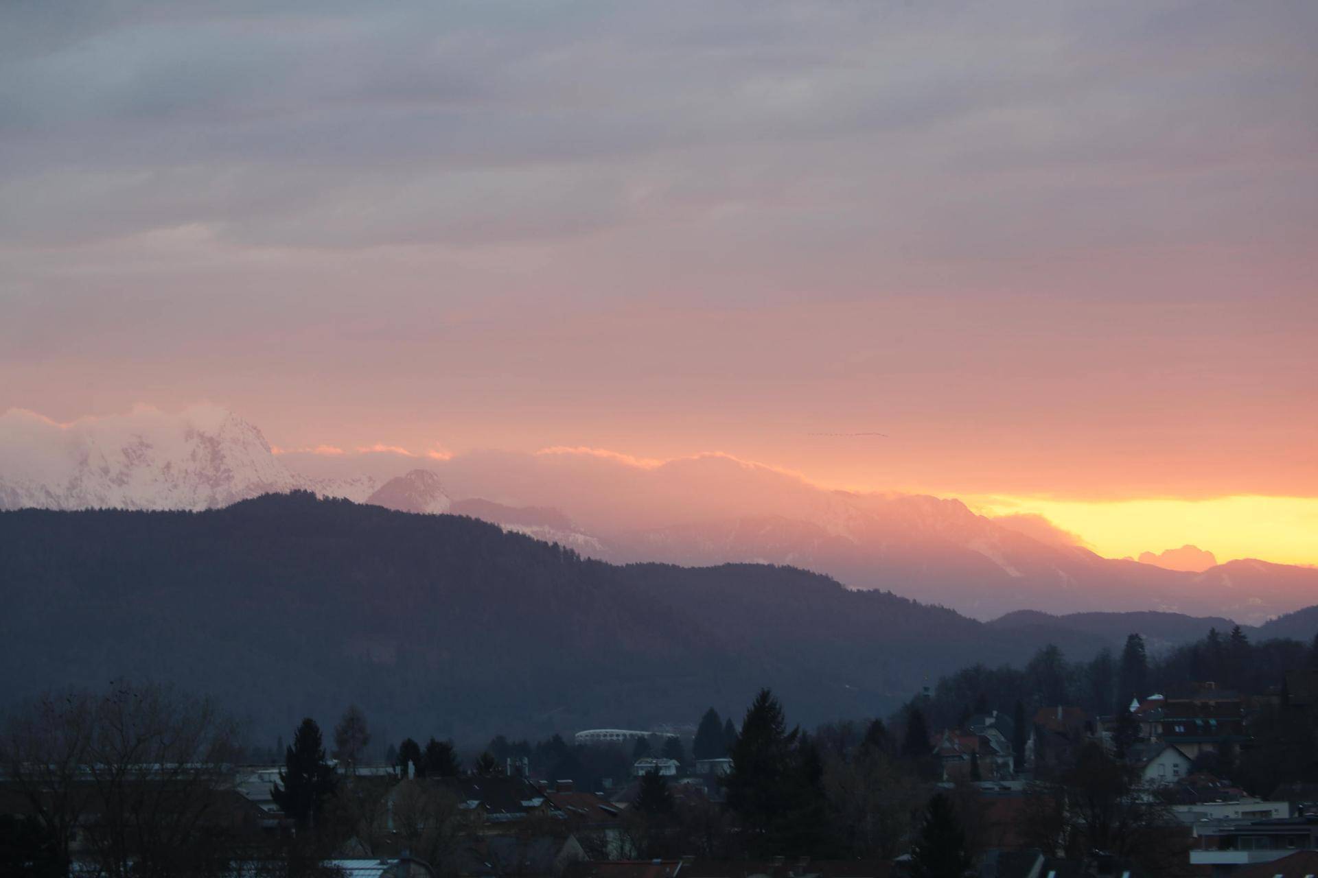 Spektakulärer Sonnenuntergang über der Stadt mit leuchtenden Farben am Horizont und schneebedeckten Bergen.
