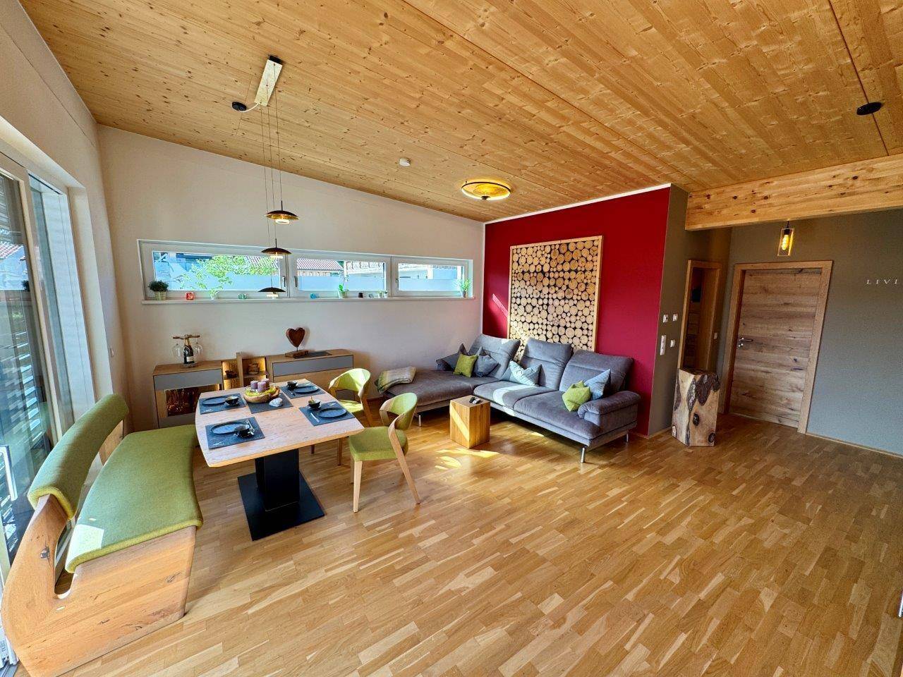 Gemütlicher Wohn-Essbereich mit Holzboden, Holzdecke und roter Akzentwand.