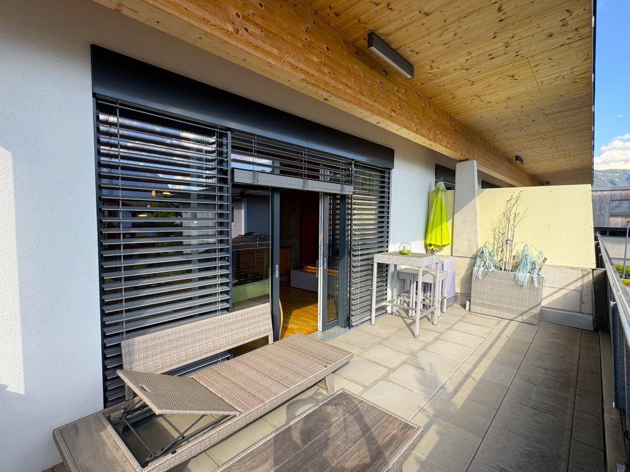 Geräumiger Balkon mit Holzdecke, Fliesenboden und bequemen Outdoor-Möbeln.