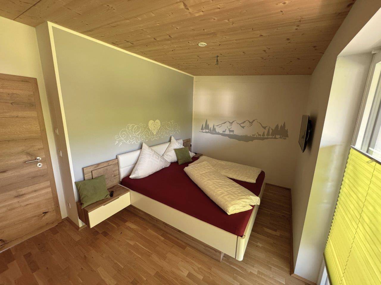 Helles Schlafzimmer mit Holzboden, Holzdecke und dezenter Wanddekoration.
