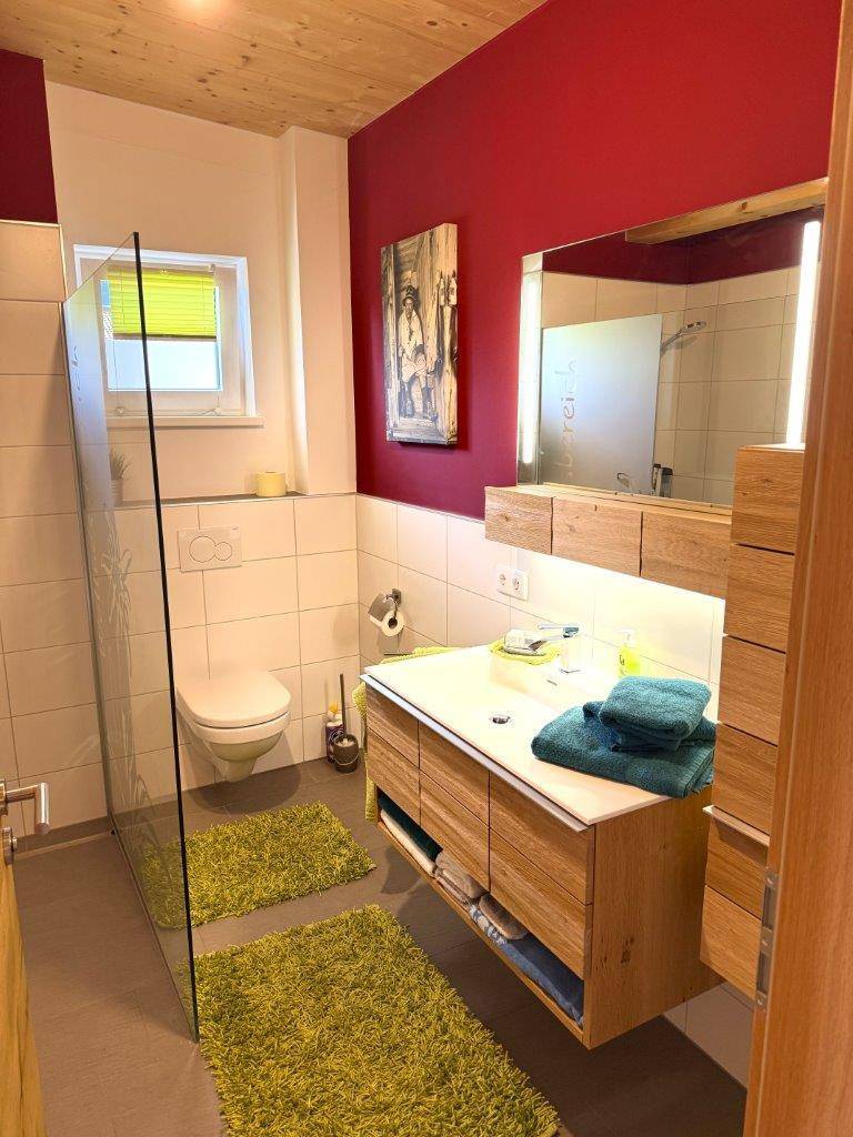 Modernes Badezimmer mit Dusche, Holzwaschtisch und roter Akzentwand.