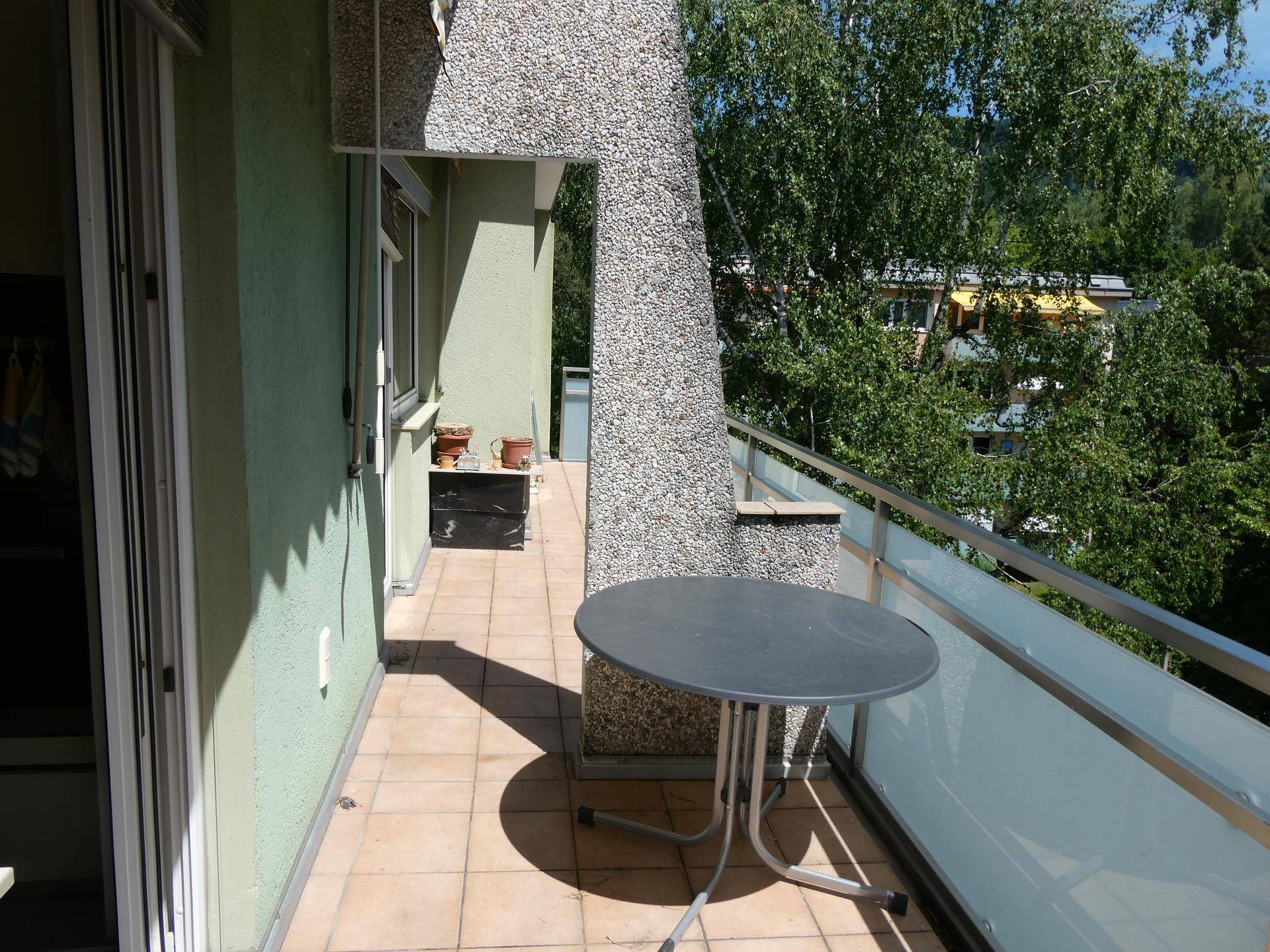 Balkon mit kleinem Tisch, Fliesenboden und Blick ins Grüne.